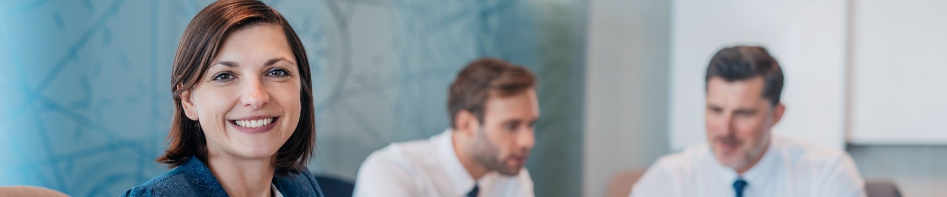 Portrait einer lächelnden Business-Frau mit im Hintergrund arbeitenden Kollegen