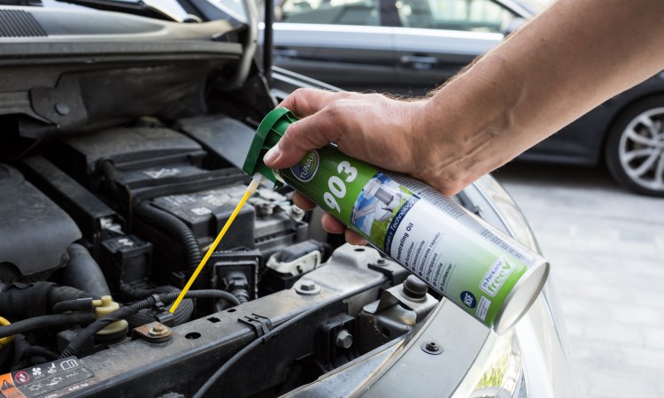 Hand sprüht Rostlöser auf verrostete Schraube im Motorraum