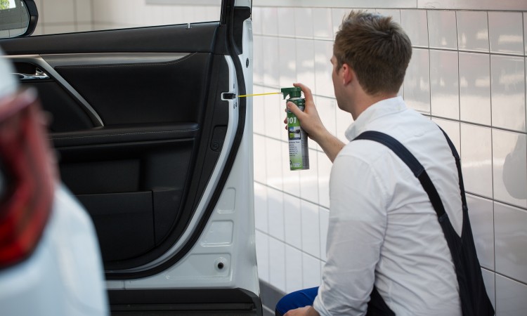 Mechaniker mit Wartungsspray an Auto zur Schmierung