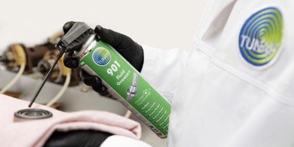 Mechaniker in der Hocke vor Autotür und Spraydose um Scharnier zu schmieren